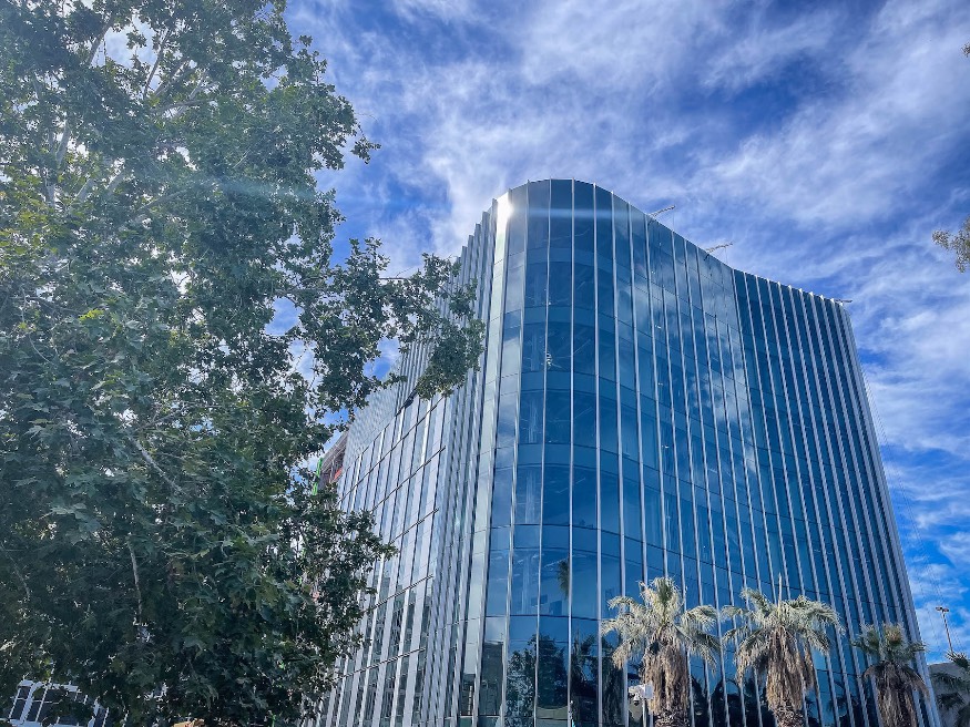 This is the main view of the SJSU Interdisciplinary Science building, which shows a rounded corner edge. It is a high-rise building covered in smooth glass that reflects the sky and clouds.